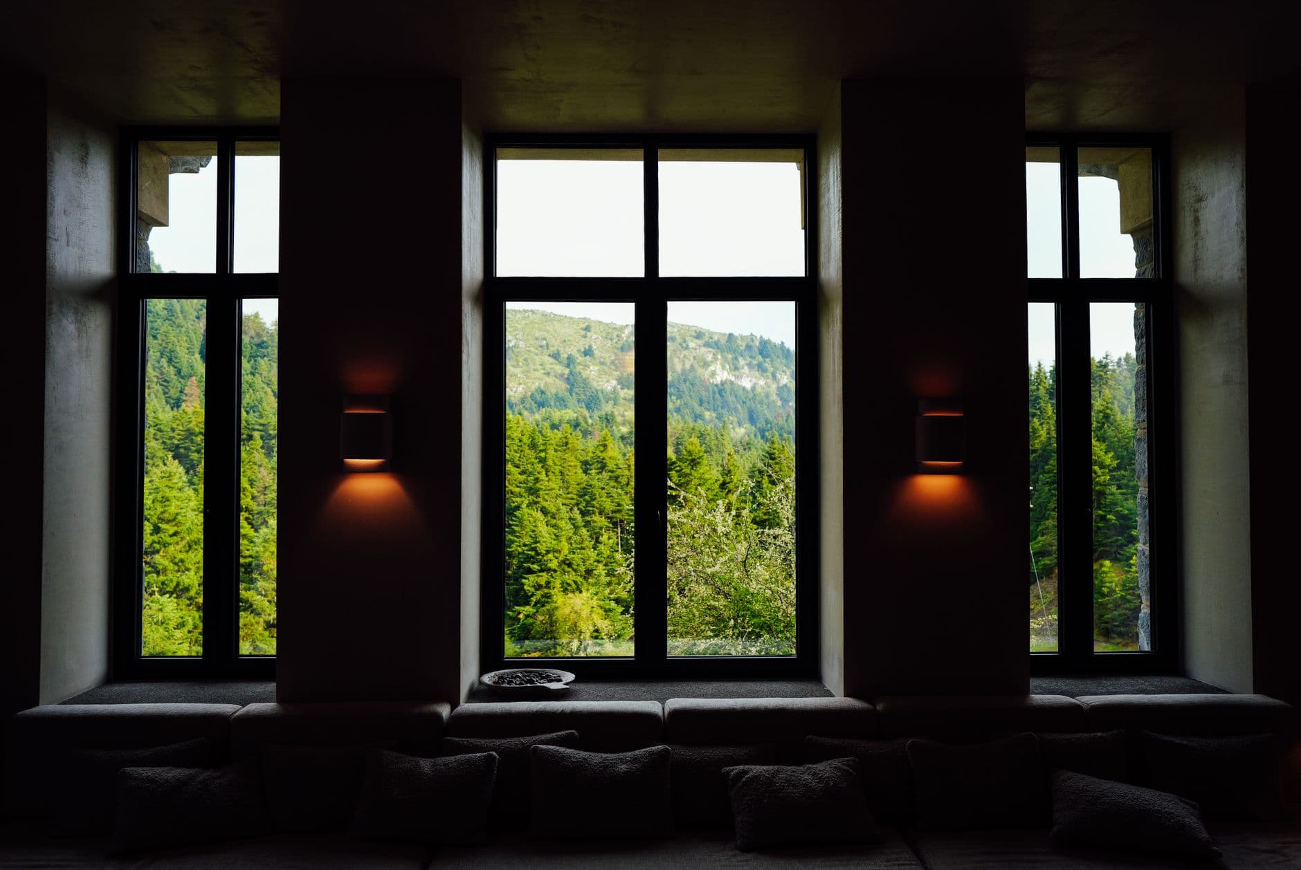 Serene forest and mountain view framed by large windows in a cozy interior setting.